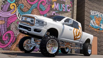 White heavily lifted show truck with orange accents in front of a graffiti wall